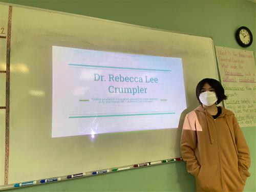 Photo of a Perry student standing in front of a whiteboard showing a projected presentation on Dr. Rebecca Lee Crumpler.